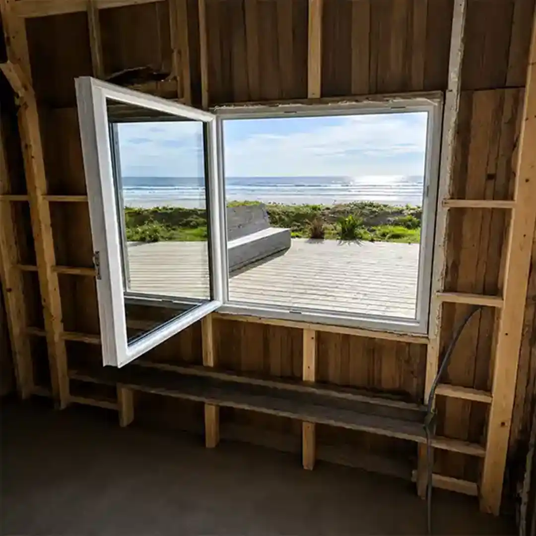 Fenêtre PVC blanche installée dans une maison en bord de mer avec vue sur l’océan depuis l’intérieur du logement.