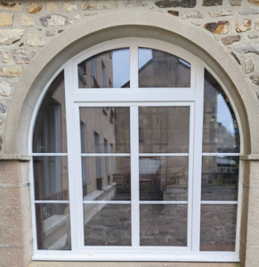 Fenêtre PVC cintrée sur mesure installée sur une façade en pierre par Performances Menuiseries